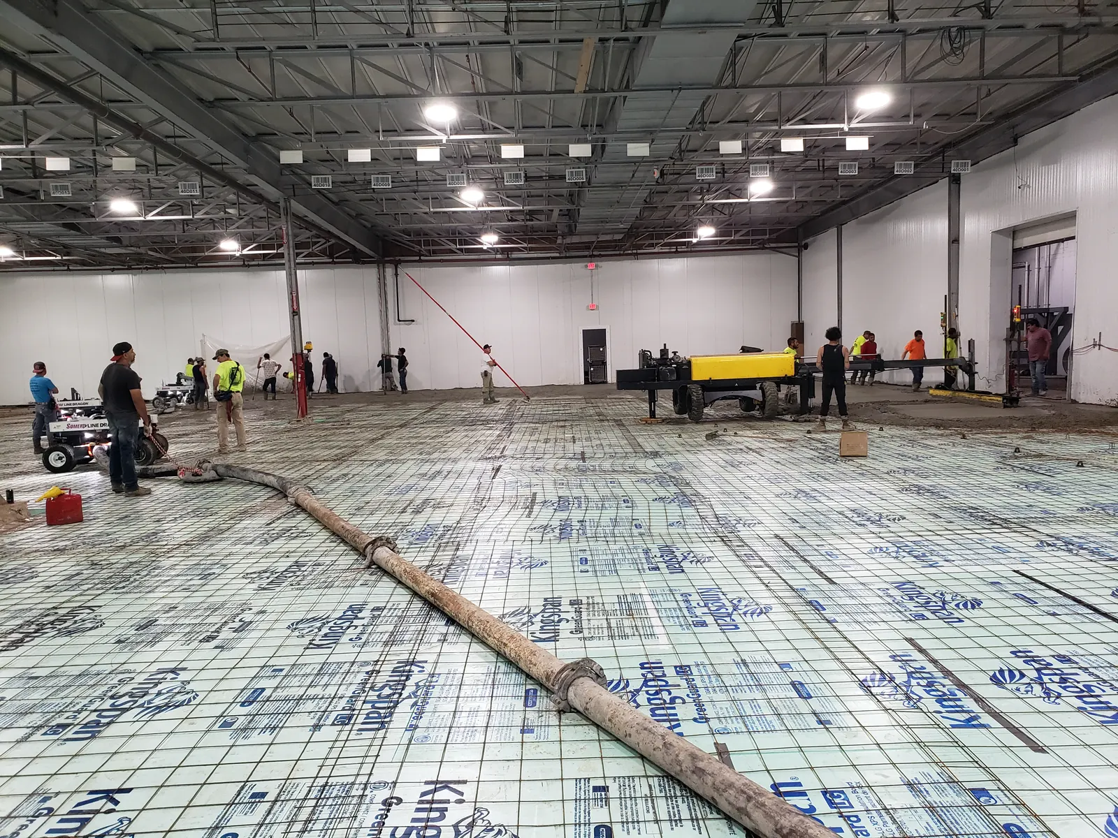 Concrete placement in a warehouse, with a hose across reinforcement and underlayment in the foreground